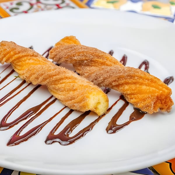 Two cinnamon sugar churros drizzled with chocolate sauce on a white plate at José's Torta Mexicana.