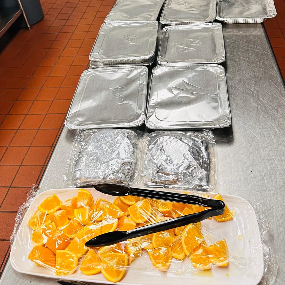 Catering trays of food and a platter of orange slices with tongs on a stainless steel counter.