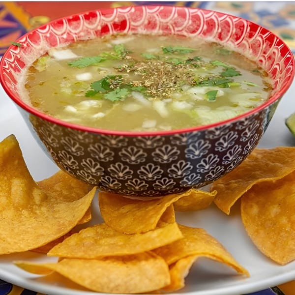 A bowl of José's Torta Mexicana pozole verde, garnished with cilantro and oregano, served with tortilla chips.