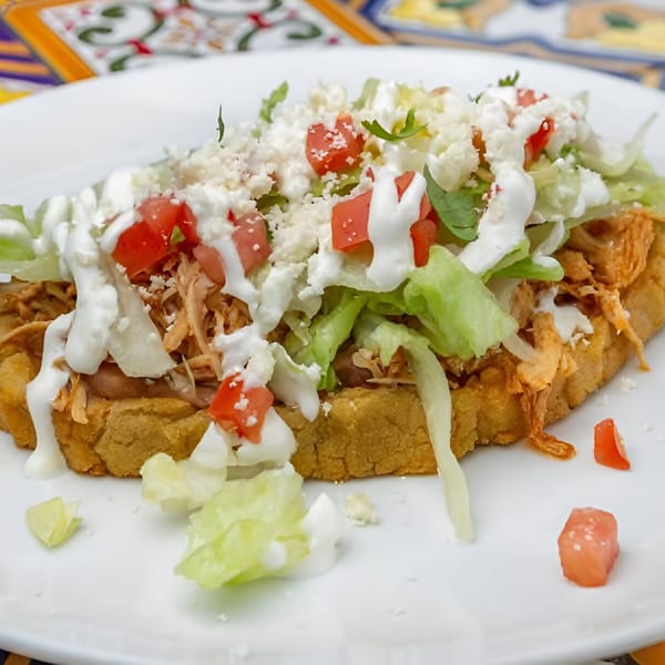 A José's Torta Mexicana sope topped with shredded chicken, lettuce, tomatoes, cheese, and crema.