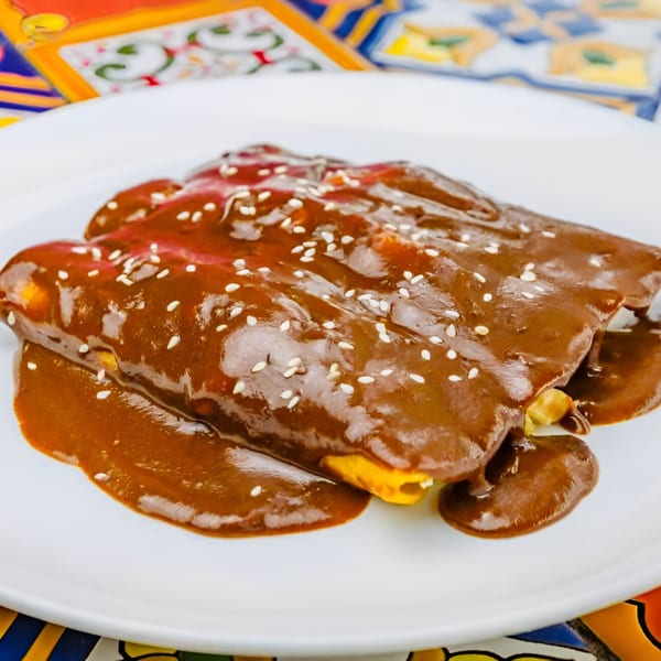Three enchiladas covered in rich mole sauce and sesame seeds on a white plate.