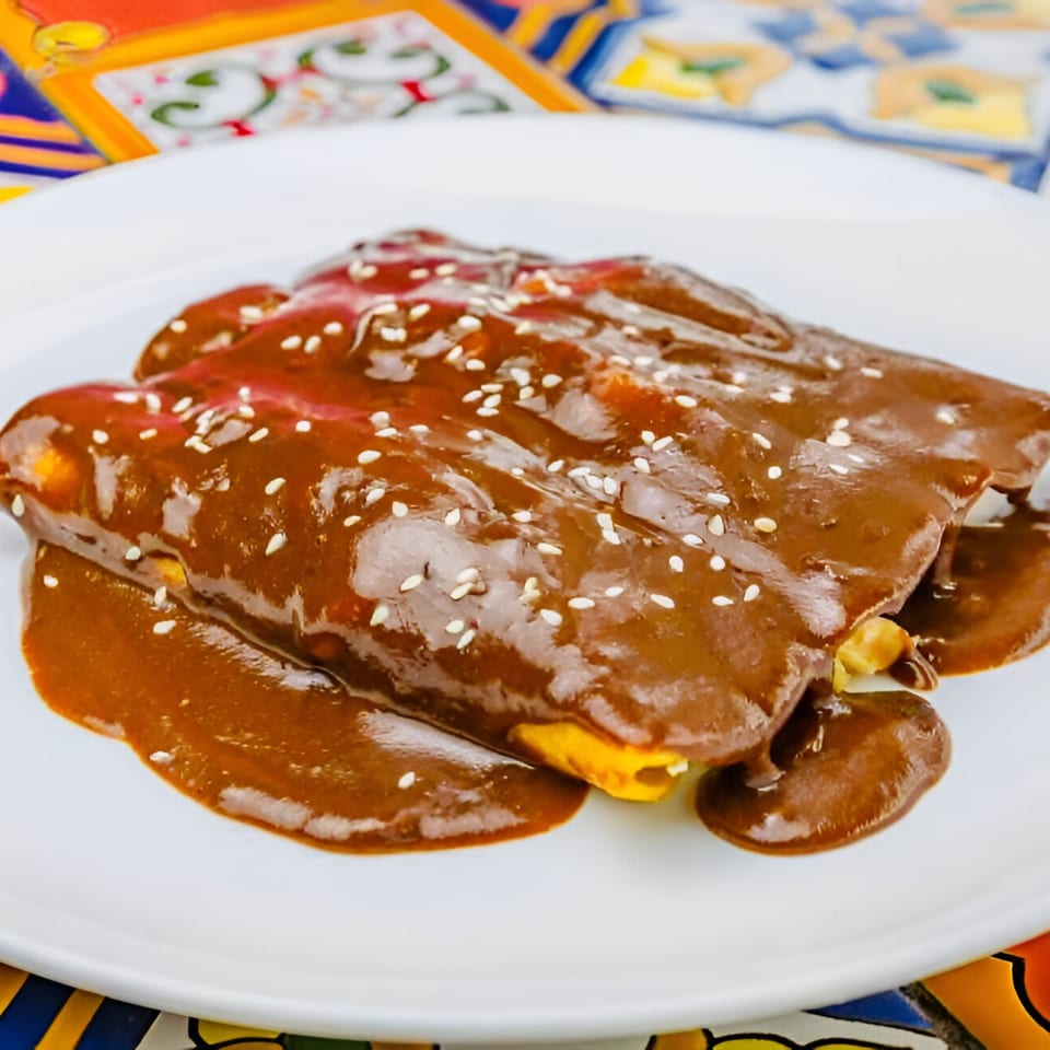 Three enchiladas covered in rich mole sauce and sesame seeds on a white plate.