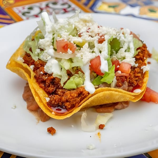 A crispy tortilla bowl filled with ground meat, lettuce, tomatoes, sour cream, and crumbled cheese.