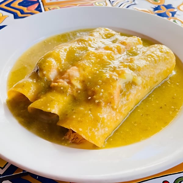 Two chicken enchiladas covered in vibrant green salsa and melted cheese on a white plate.